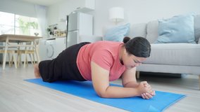 Asian young oversize woman doing yoga exercise in living room at home. Attractive plus size girl workout by follow Pilates instruction video from online trainer on television to lose weight in house.
