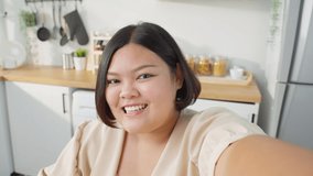 Asian oversize vlogger big woman eat unhealthy food in kitchen at home. Young attractive beautiful plus size fat girl hold camera and record video live streaming by bite sweet donut on table in house.