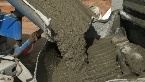 Concrete is poured from a concrete mixer into a metal container on construction site. Cement truck pours wet heavy concrete. Construction works, preparation for pouring foundation of a building.