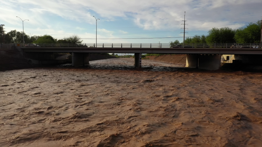 Drone View Of Raging River After Monsoon Storm With Brown Water Flowing Under Road Bridge. Santa Cruz River In Tucson, Arizona. pullback