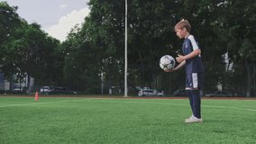 SLOW MOTION - Boy trains professionally on a football field with a ball. Training with a ball on football pitch while sunset. Active child makes a feint with football on a green field. Sport concept