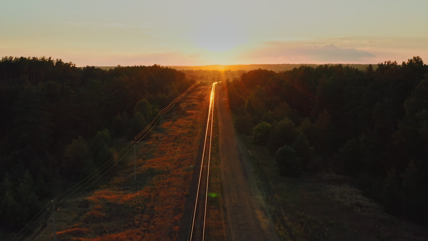 Drone flying forward over railway track while beautiful sunset. Suburban railway during sunrise in summer. Sun rays of the setting sun are beautifully reflected from the railway rails. Travel concept. Royalty-Free Stock Footage #1076883641