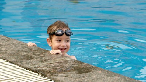 Cheerful little boy in goggles bathing in the pool. Cute child little baby boy in the pool in swimming goggles, kid jumps in the pool.