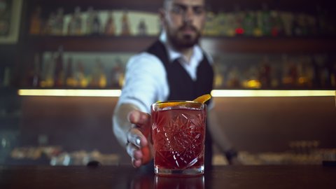 Bartender serves the visitor a red cocktail with an orange - negroni, the hand takes a glass.