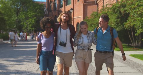 Dolly shot of cheerful multiethnic travelers walking in summer city. Young happy diverse students n summer vacation travel together abroad and sightseeing in european city