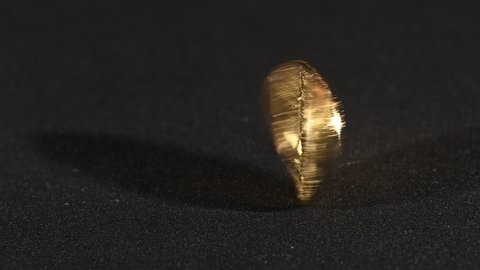 Close up one golden bitcoin physical coin spins and falls over black background with copy space, slow motion