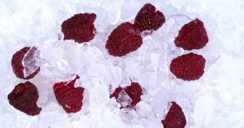 Slow motion of ice cubes fall on top of red and fresh raspberries on ice, a delicious and natural dessert with vitamins. Filmed high speed cinema camera. 4K.