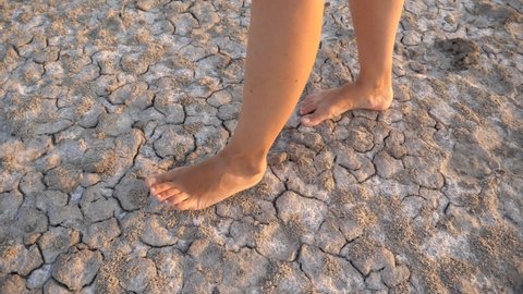 Barefoot woman legs walking on very dry cracked soil ground on hot summer climate