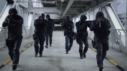 Front view special forces team moving on bridge at urban building. Serious squad of SWAT police in military uniform using modern rifles during special operation. Special ops police team in action