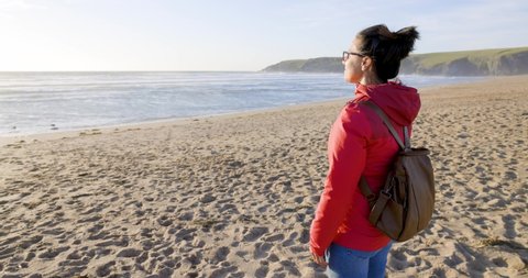 Woman with backpack looking at the sea with arms outstretched