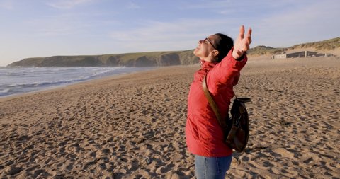 Woman with backpack looking at the sea with arms outstretched