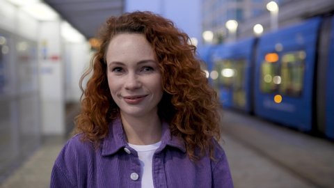 Young woman standing at train station, looking at camera