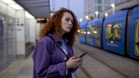 Young woman with smartphone standing on platform waiting for train