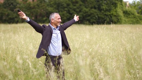Happy businessman with smartphone dancing in meadow