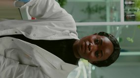 Vertical video: Pov of african woman sitting at desk table in pharmaceutical laboratory during online videocall meeting. Specialists team researching genetic mutation developing dna GMO biology test