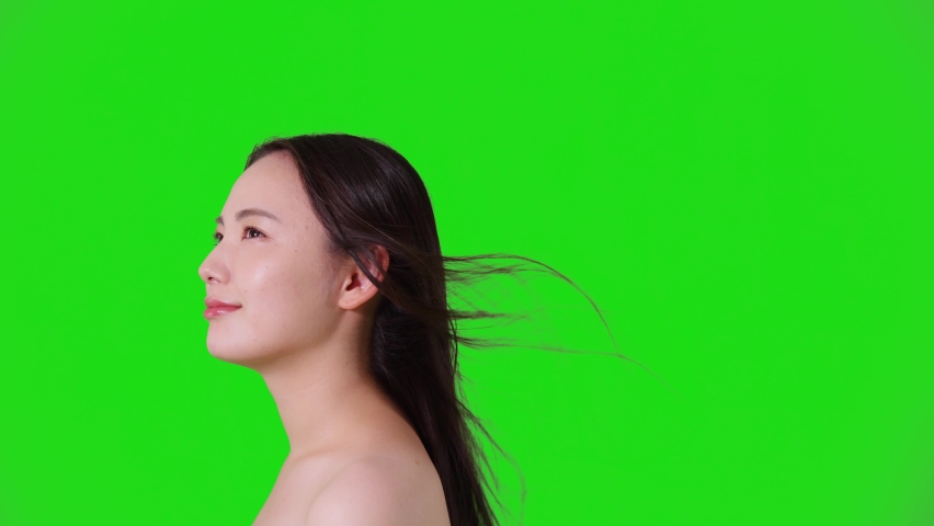 Young asian woman blowing her hair. Hair care concept. Green background for chroma key composition.