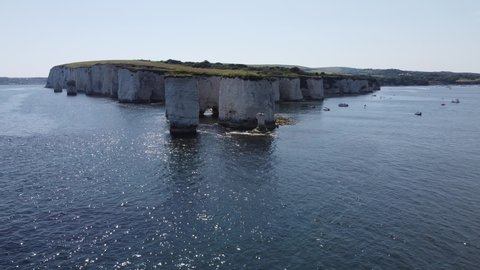 Drone shot of Old Harry's Rocks in Dorset, England - large chalk stacks and cliffs with tourists involved in outdoor water sports (kayaking, boating, paddle boarding) in the coves and ocean water 