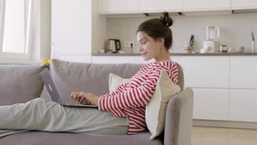 Happy young girl blogger communicating, chatting by webcam online on laptop distantly on sofa at home. Smiling caucasian girl make video call, interact using social networks apps on computer.