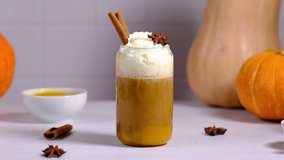 A woman pours caramel syrup over a pumpkin latte and sprinkle with cinnamon.