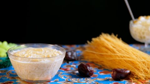 An Indian woman garnishing a bowl of tasty homemade Sevai with almonds. Raw Seviyan vermicelli, dates for Eid feast. Festival mood, Festival celebration