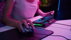 Woman gamer hands using wired computer mouse and typing on neon keyboard, playing video games at night close-up. Professional skills of cybersport. Gaming club concept. 