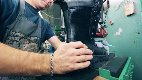Leather boot is getting put into its sole by a factory worker. Worker sewing shoes. Footwear factory facility.