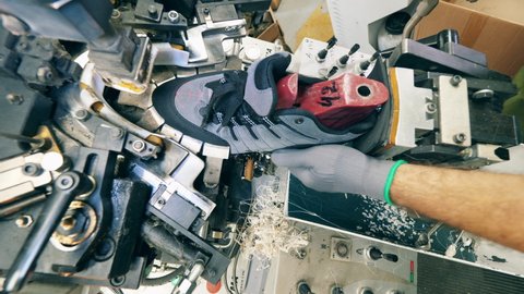 Footwear factory worker making shoes. Lasting machine is being used to shape a new boot