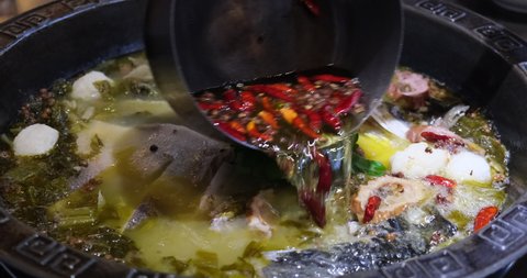 Pouring hot boiling chili oil into fish soup and pickled cabbage. Slow motion. Cooking Chinese cuisine concept. Boiled fish with pickled cabbage and chili is a traditional Chinese food