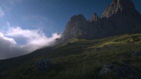 Wide dynamic range panorama of a rocky mountain with clouds surrounded by green grass in the evening before sunset. Intense frame from raw video