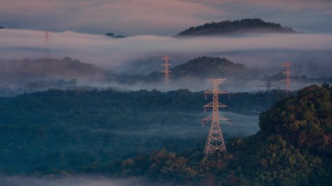 Time lapse Aerial view high voltage power transmission towers or electricity pylon in fog on mountain mae moh lampang.
