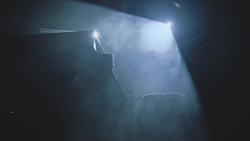 Professional pianist in dark suit playing on a grand piano on big stage in concert hall with dimmed light in the smoke. Concept of sound and music