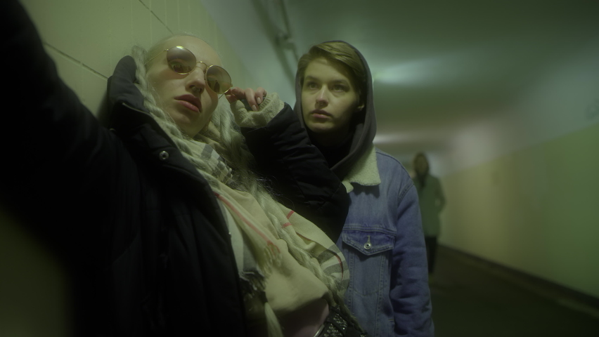 Two girls in the underpass take selfies on their phone, people pass by, a graffiti artist draws on the wall, then everyone runs away from the police.