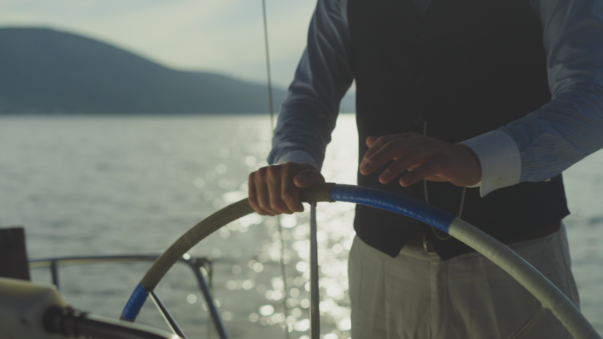 Male hands turning with steering wheel on boat. Man driving yacht on water. Summer vacation at sea, sailing and travelling concept. | Shutterstock HD Video #1076963279