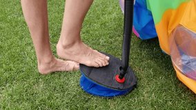 a man's leg pumps air with a pump, inflates an outdoor paddling pool. Green grass.