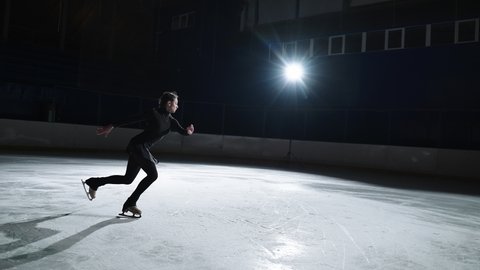  Female artistic figure skater is performing a woman's single skating choreography on ice rink before start of a competition. Slow motion 120 fps. Concept of perfection, precision, freedom, passion