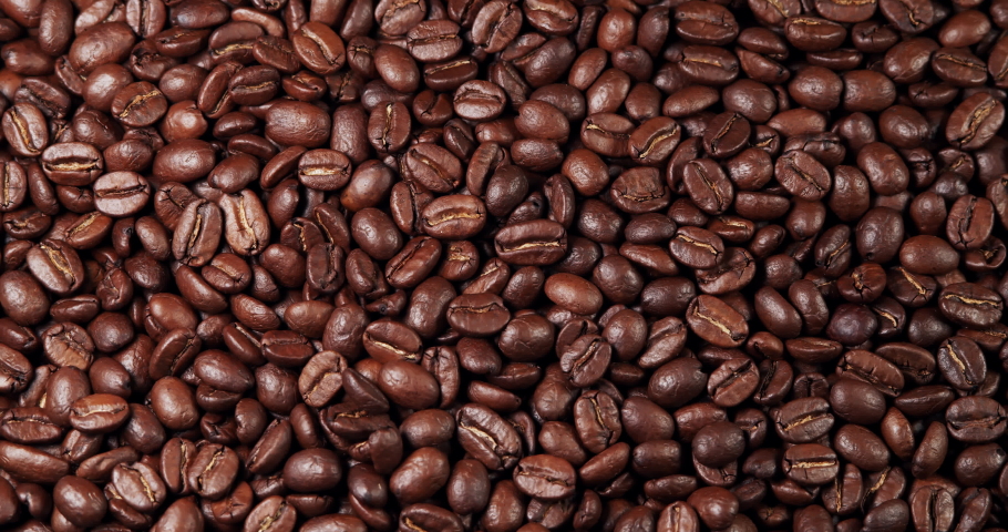 Roasted coffee beans. Aromatic coffee beans move slowly. Slow motion close-up of whole roasted coffee beans.