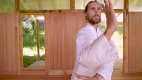 Bearded caucasian man wearing white clothes to practice concentration and breathing before practicing qigong tai chi