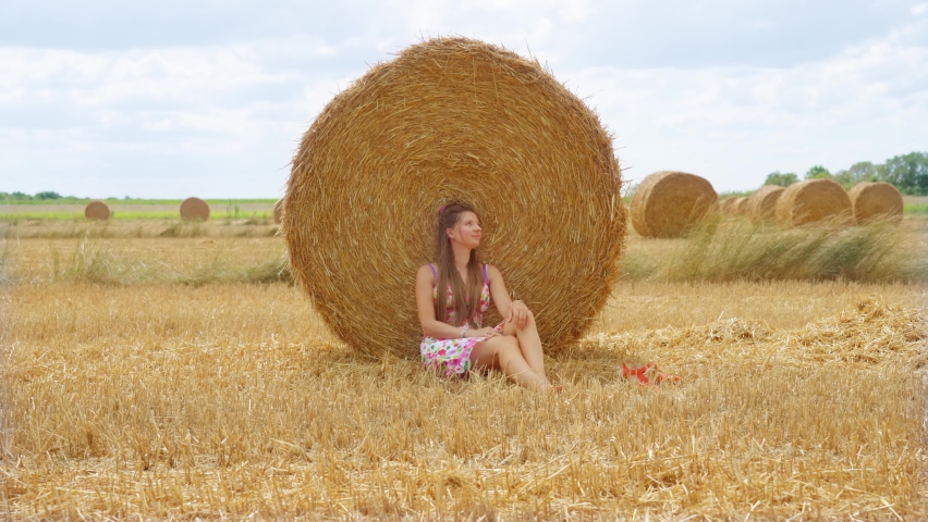 Woman sitting in front of yellow haystack on the summer field