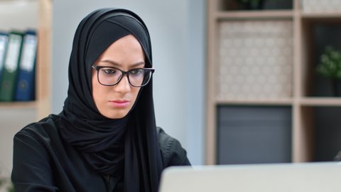 Closeup focused young Muslim business woman in black headscarf working chatting surfing internet use laptop. Confident modern Saudi lady studying remotely e learning distance education on computer