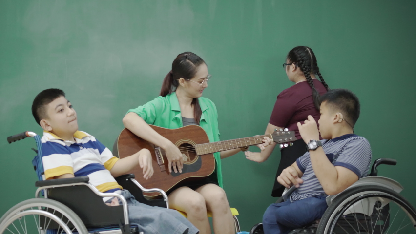 Group Asian Children with disabilities in wheelchairs and autism singing activities teacher playing guitar in classroom. Activities to enhance learning skills. Education for disadvantaged children Royalty-Free Stock Footage #1076989760
