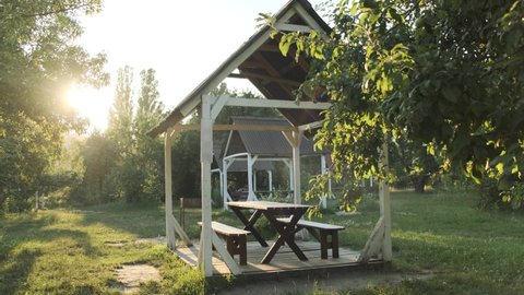 Empty gazebo for rest and picnic next to the barbecue in the park during sunset. Wooden summer house for vacationers in the forest