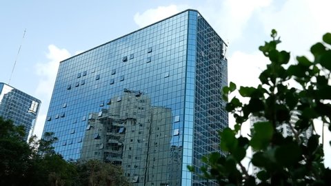 A reflection a building upon a glass covered bluish building, with an out of focus bush in the foreground, slight slow motion, Ramat Gan, Israel.