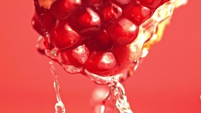Super slow motion with a piece of pomegranate drains water. On a red background. Filmed on a high-speed camera. High quality FullHD footage