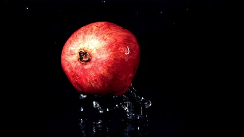 Super slow motion one ripe pomegranate falls on the water with splashes. On a black background. Filmed on a high-speed camera at 1000 fps. High quality FullHD footage