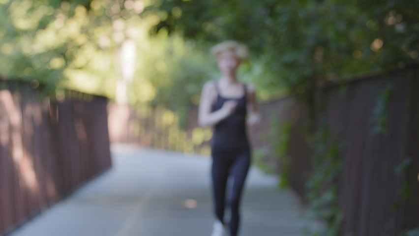 Athletic strong active woman slim lady runner female jogger trainer sportswoman running in park on bridge outdoors doing morning jogging cardio exercise sports workout feels tired exhaustion stops