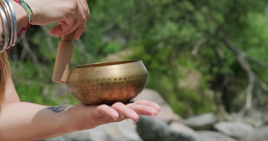 Ringing Tibetan Bell. Female Hand Circling The Rim Of A Bowl With A Baton And Strike. close up