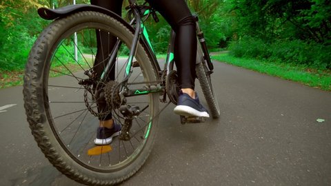 The bike rides on an asphalt road in the middle of the forest. Close-up of the legs and wheels. The gearshift mechanism turns and the chain rotates. Dynamic shooting from a steadicam.