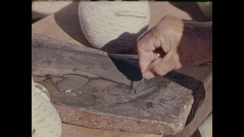 1970s: Hand wetting brush in paint, painting design on vessel. Woman inspecting painted vessel. Woman placing clay creature into fire pit, placing rock nearby.