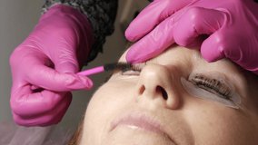 Adult woman face on modern eyelash lamination procedure in professional beauty salon. Master apply black dye paint to the eyelashes during the eyelash curling procedure with a special brush close up.