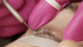 Adult woman face on modern eyelash lamination procedure in a professional beauty salon. The master applies special glue before the eyelash curling procedure in pink rubber gloves close up